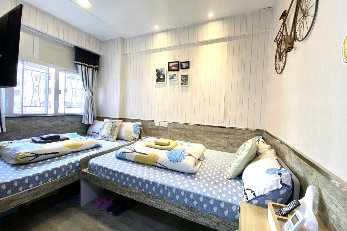 A room with two beds, a mounted bicycle, a TV, and a window with curtains.