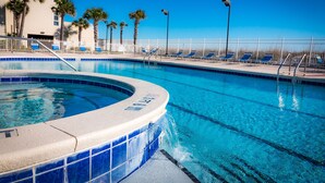 Une piscine avec un jacuzzi, des chaises longues, des palmiers et une clôture blanche.