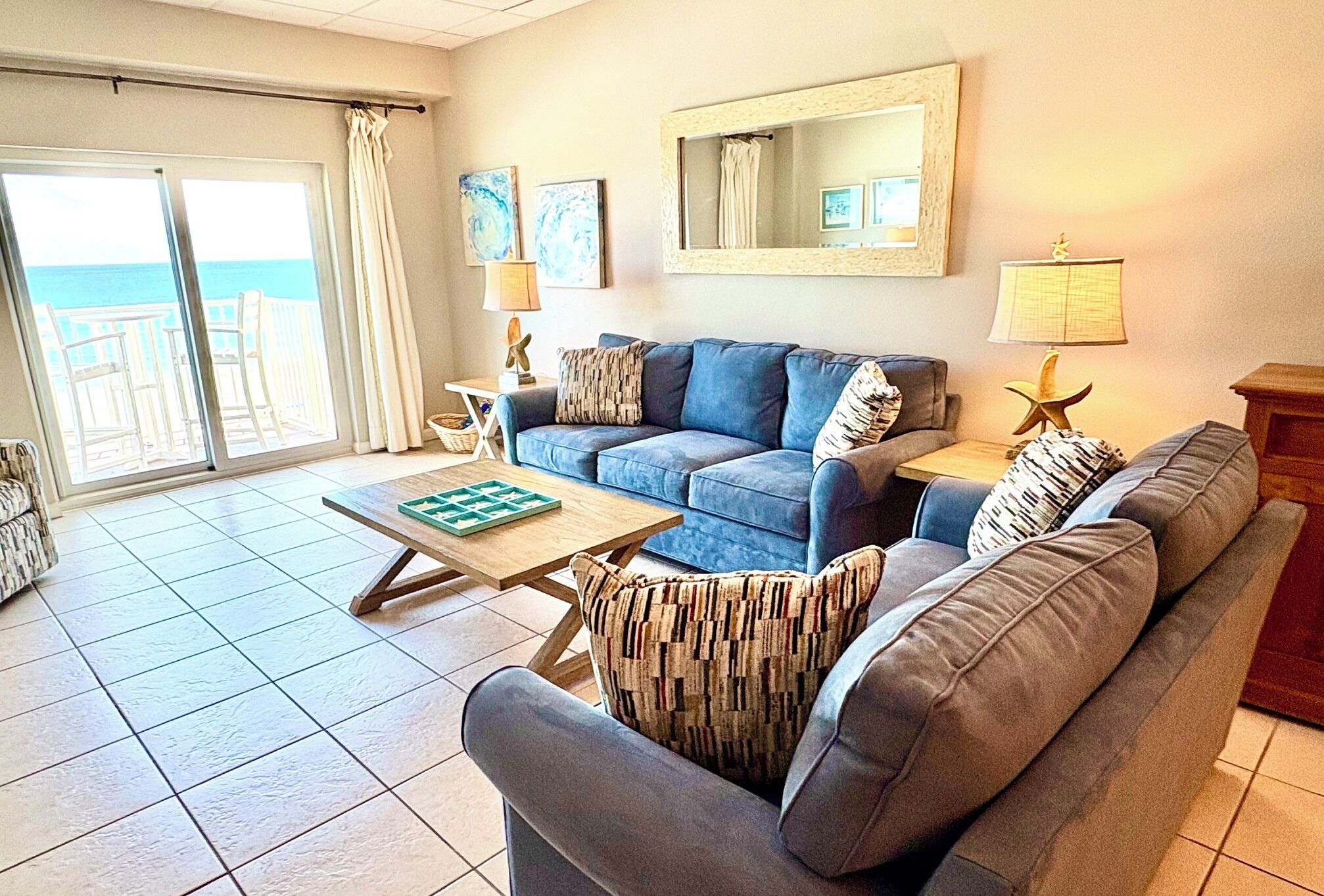 A living room with a blue sofa, a wooden coffee table, and a view through a sliding glass door to the outside.