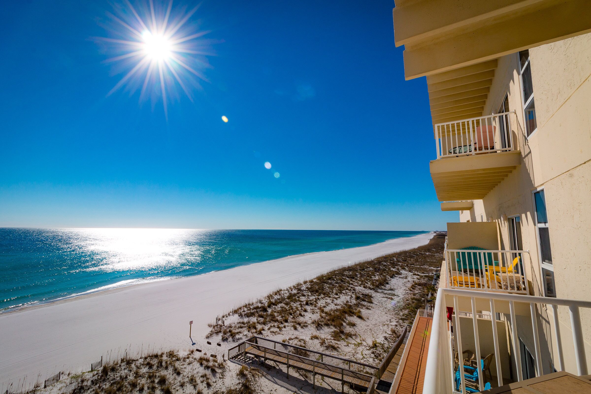 Un hôtel situé en bord de mer, doté d’un balcon avec vue sur l’océan, d’une plage de sable et d’un ciel dégagé.