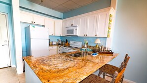 Une cuisine avec des meubles blancs, un plan de travail en granit, une cuisinière et un four à micro-ondes.