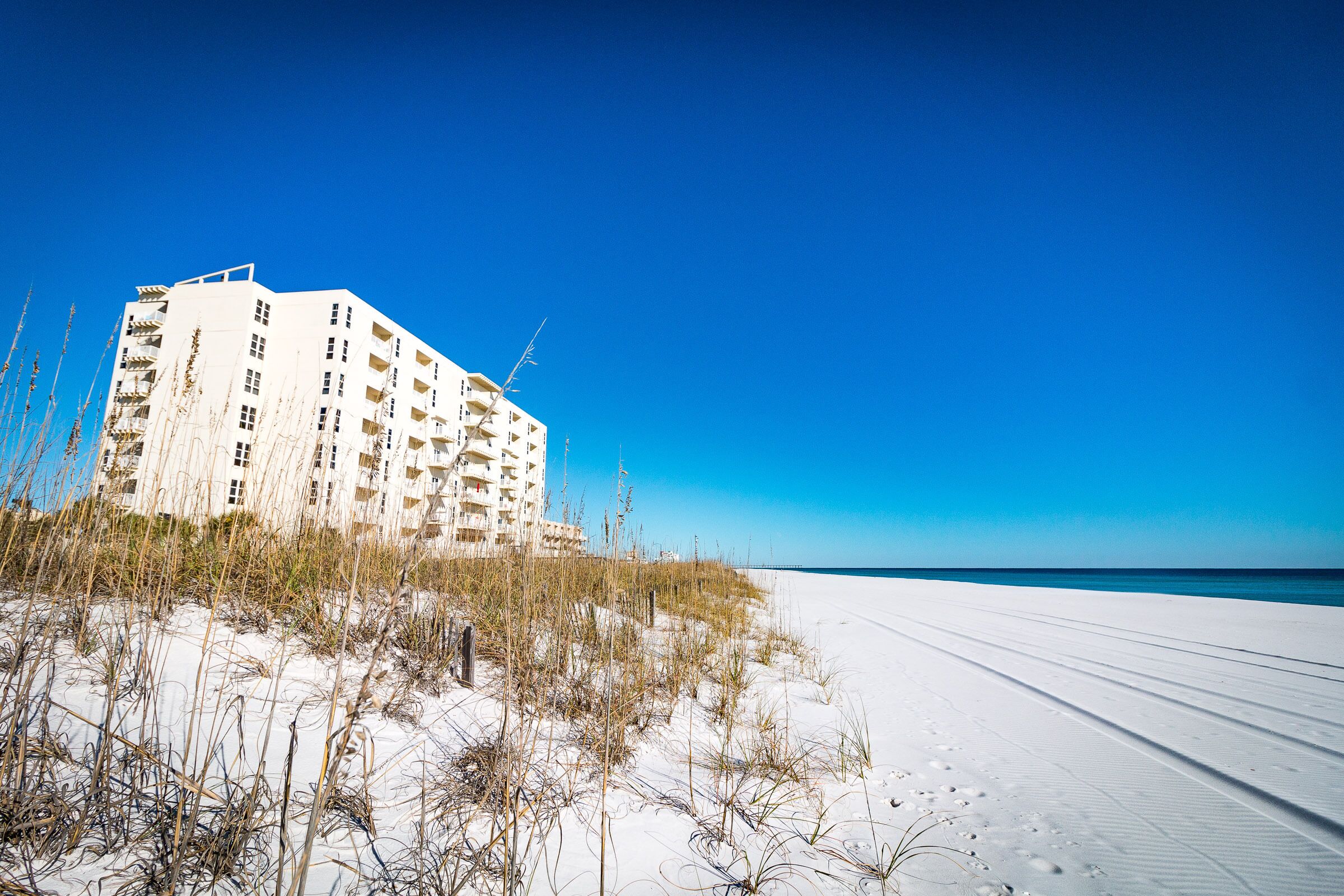 A beachfront hotel with multiple floors, located on a sandy beach with sparse vegetation.