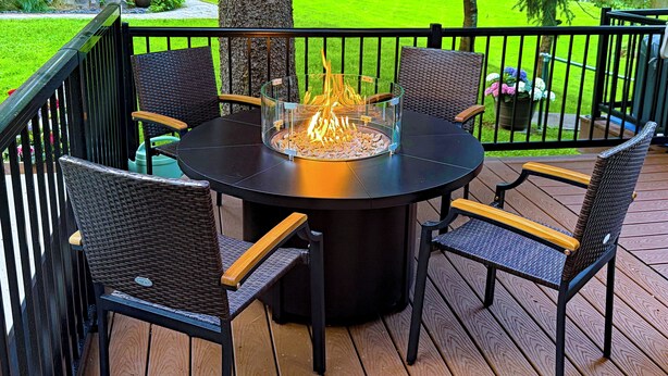 A round outdoor table with chairs, a fire pit, and a deck railing. - WATER FRONT- Cozy Country Home SPA, Pristine Lawns, wildlife & trails to Explore (Spokane)