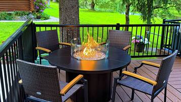 Une table ronde d’extérieur avec des chaises, un foyer et une rambarde de terrasse.