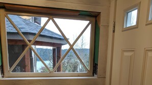 Une pièce dotée d’une porte en bois, d’une fenêtre à croisillons et offrant une vue sur un bâtiment dont le toit est en pente.