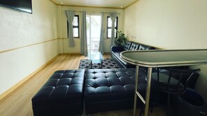 A modern living room with a black leather sofa, a glass dining table, and a view of the outdoors through large windows. - Mango's Beachfront Resort (Olongapo)