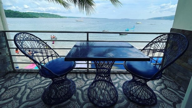 A balcony with a table and chairs overlooking a body of water with boats and people. - Mango's Beachfront Resort (Olongapo)