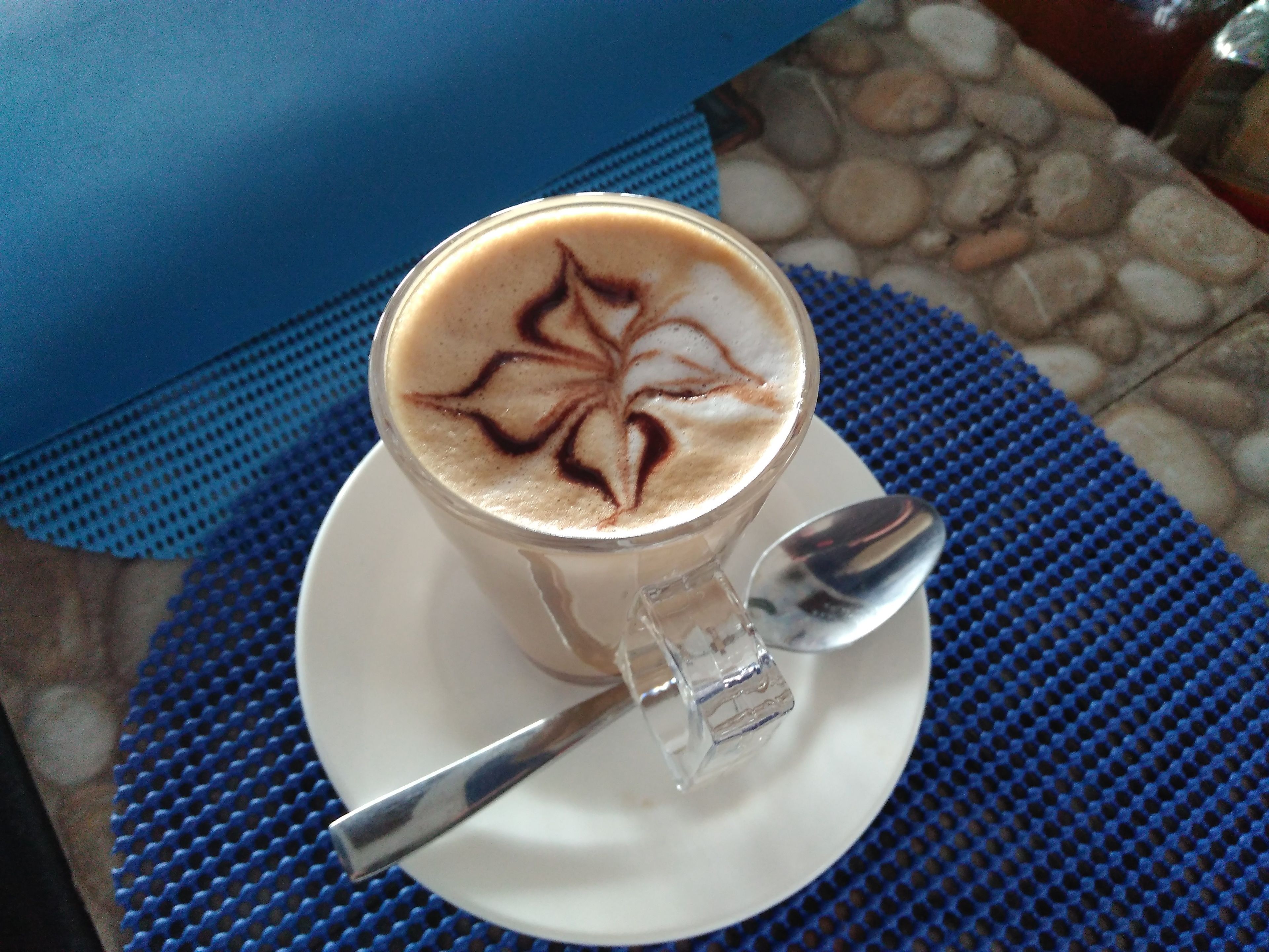 Een kop koffie met latte-art op een schoteltje, geplaatst op een blauwe, gestructureerde mat.