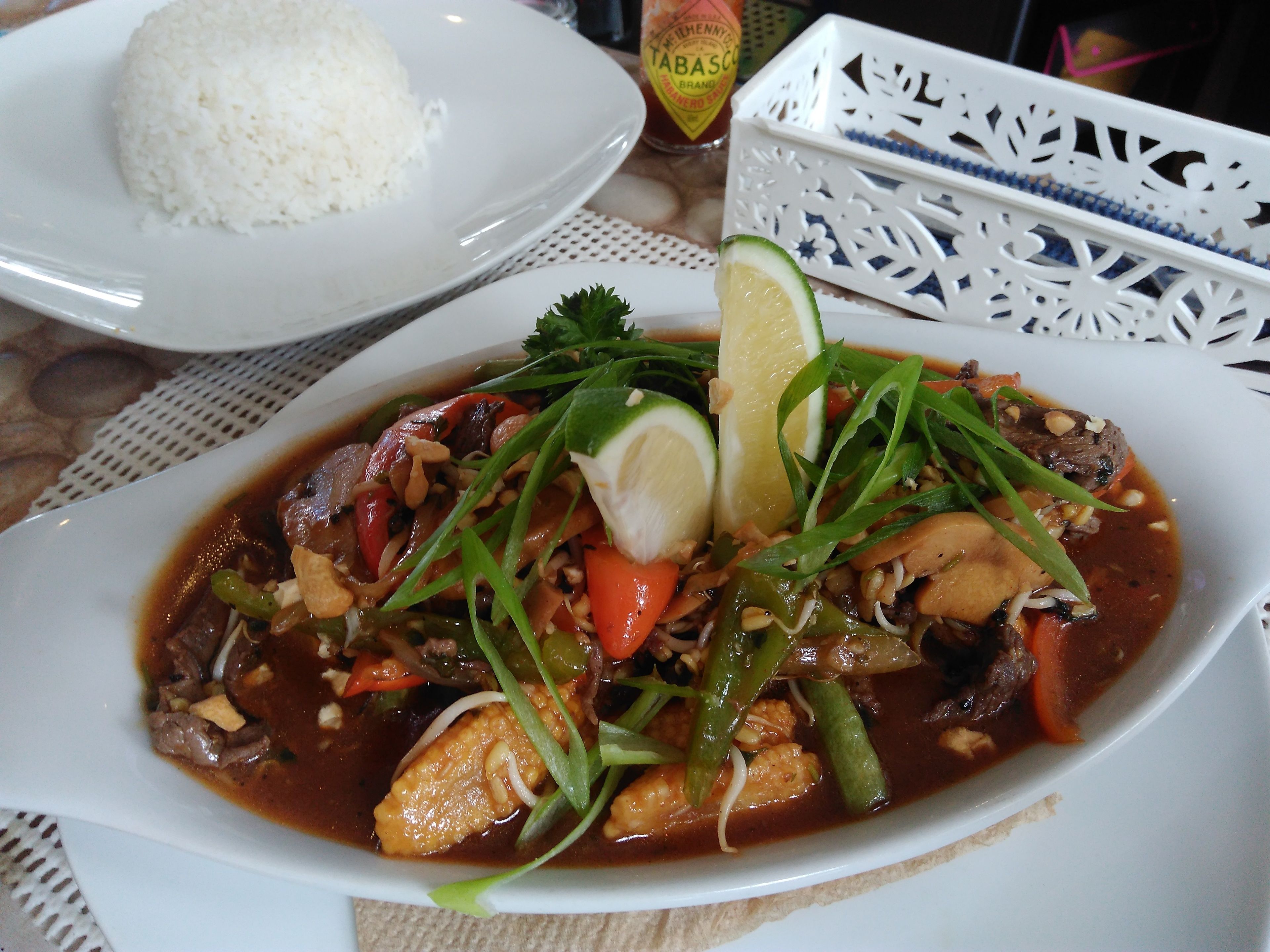 A plate of food with rice and a bowl of soup garnished with lime and green onions.