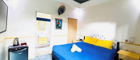 Une chambre d’hôtel avec un lit, un petit bureau, une chaise, un miroir, un tableau au mur et un petit radiateur.