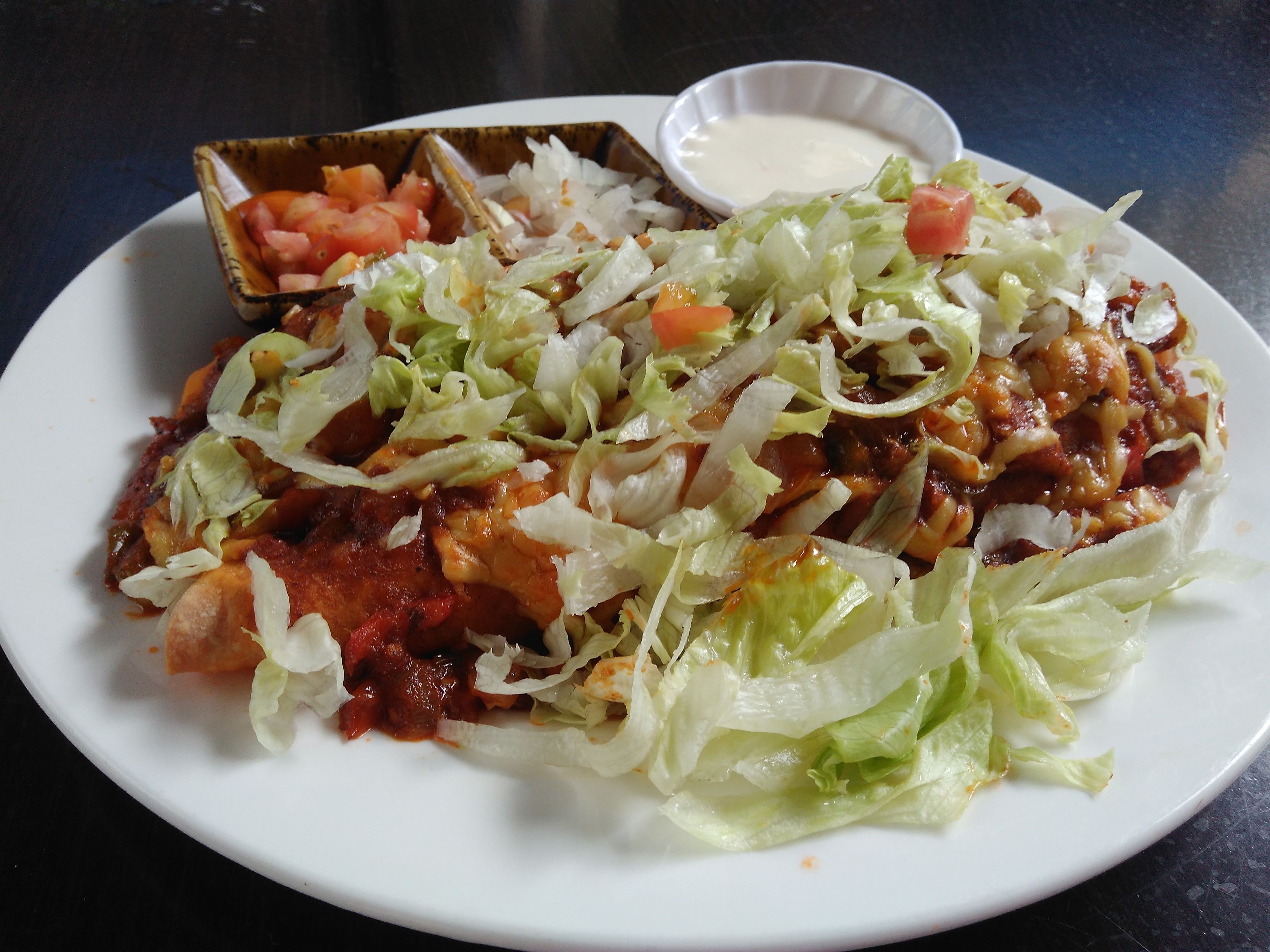 A plate of nachos topped with cheese, lettuce, and tomatoes, accompanied by a small bowl of sauce.