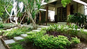 Un patio con zona de estar techada, rodeado de plantas y árboles.