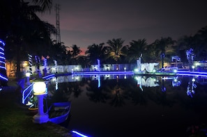 Vista nocturna de una masa de agua con senderos iluminados y palmeras.