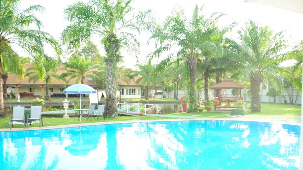 A swimming pool with a clear blue water surface, surrounded by palm trees and a gazebo. - Blue Lagoon Pool Villa (Pattaya)