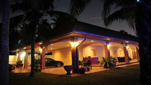 A well-lit house with a covered patio, palm trees, and a car parked outside. - Blue Lagoon Pool Villa (Pattaya)