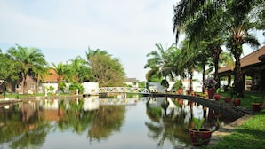 A calm water body with a bridge, surrounded by palm trees and potted plants. - Blue Lagoon Pool Villa (Pattaya)