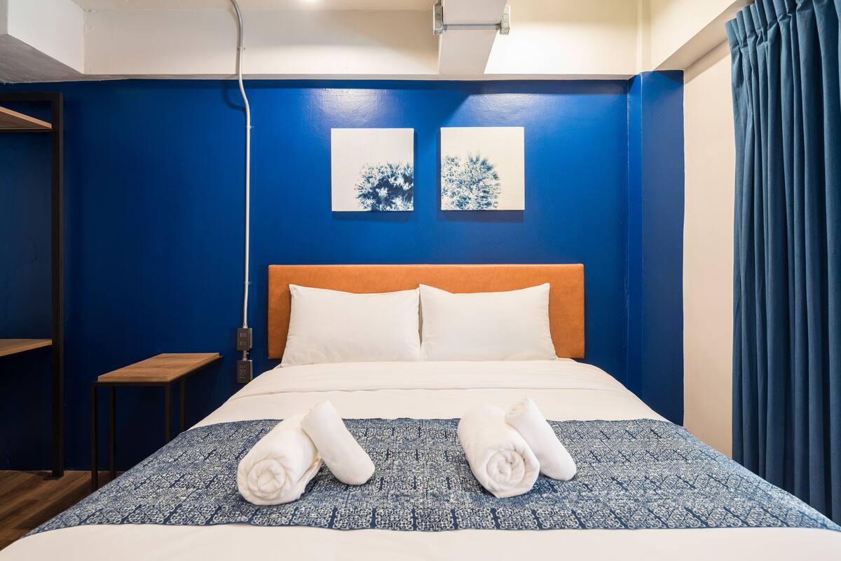 A hotel room with a blue accent wall, a wooden headboard, white bedding, and two artwork pieces above the bed.