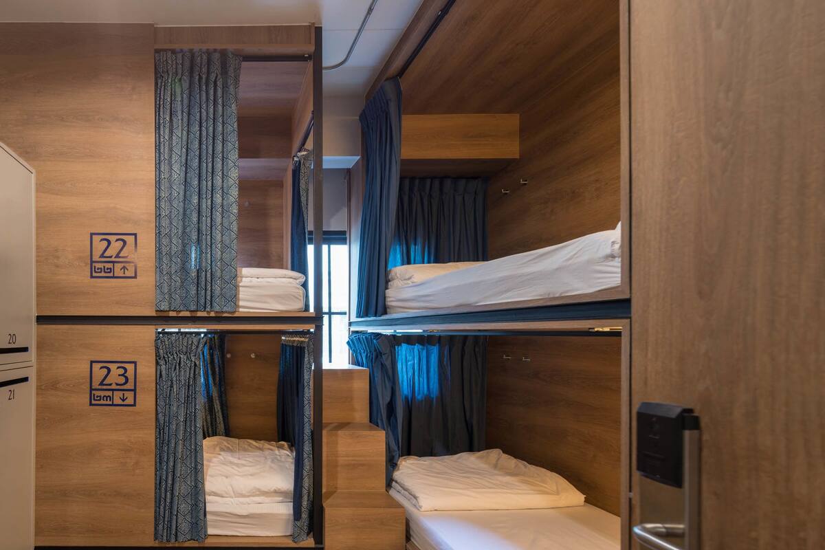 A compact, wooden-themed room with bunk beds, numbered room signs, and a small window with curtains.
