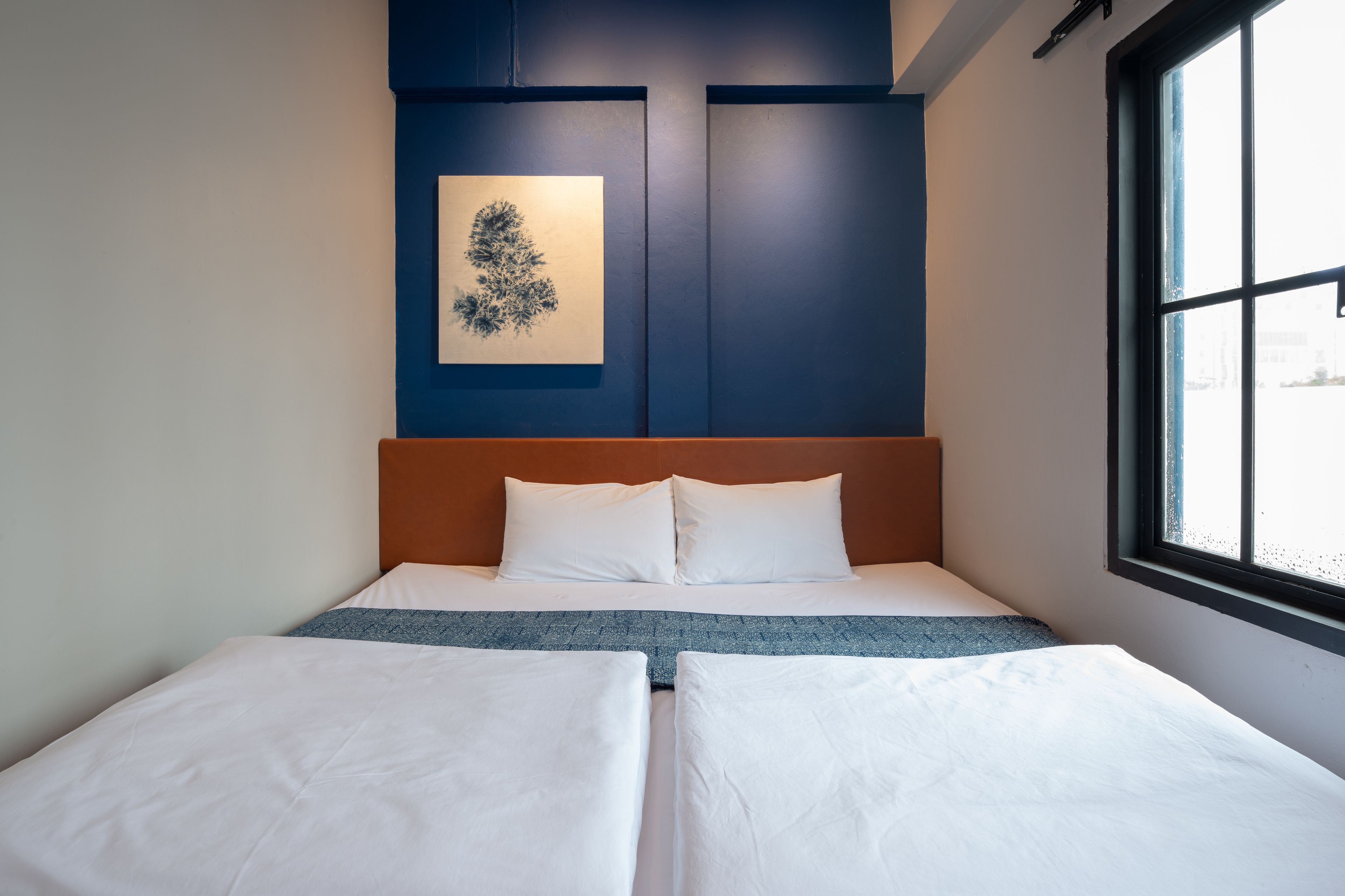 Una habitación de hotel con una cama, una ventana y una obra de arte colgada en la pared.