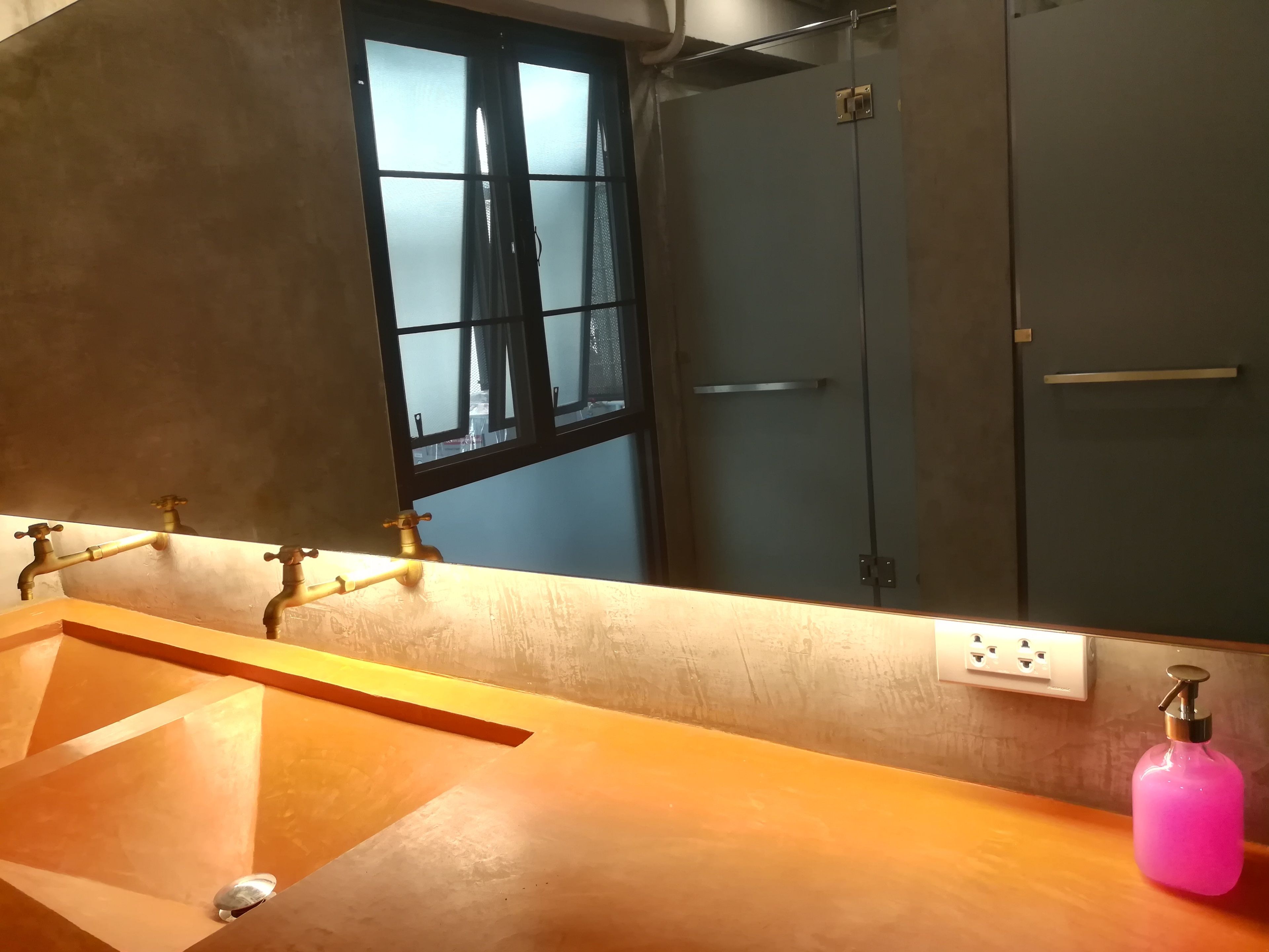 A bathroom with a wooden vanity, a mirror, a window, and a shower door.