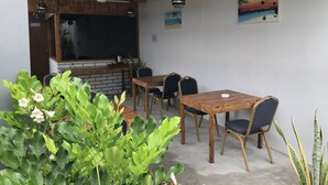 An outdoor patio with a wooden table and chairs, a ceiling fan, and a brick wall with a blackboard. - Royal Stay Inn (Thoddoo)
