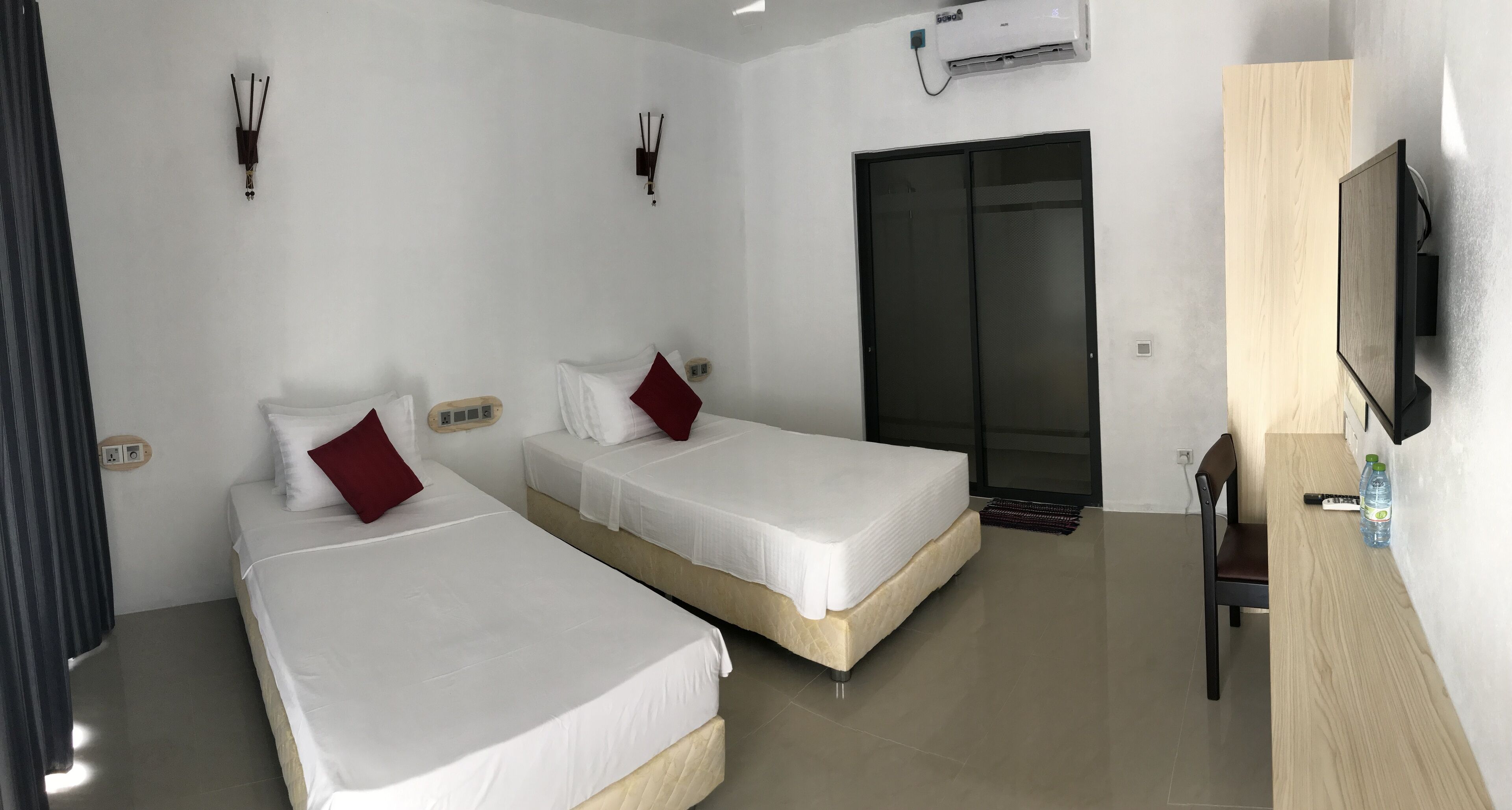 A hotel room with two beds, a TV, a wardrobe, and a desk with a bottle.
