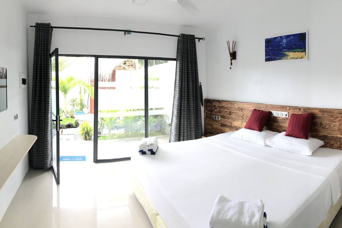 A hotel room with a large bed, a wooden headboard, a night sky painting, and a view of the outdoors through a sliding door.