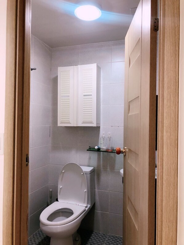 A small, clean bathroom with a toilet, a white cabinet, and a glass shelf with toiletries. - Sarang Guesthouse Dongdaemun (Seoul)