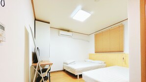 A small, clean room with two single beds, a desk, and a chair.