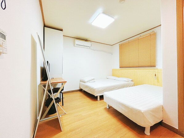 A small, clean room with two single beds, a desk, and a chair.