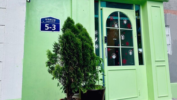 A building with a green facade, a blue sign reading "5-3", and a small tree in a planter.