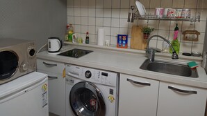 A compact kitchen with white cabinets, a built-in microwave, a washing machine, and a sink.