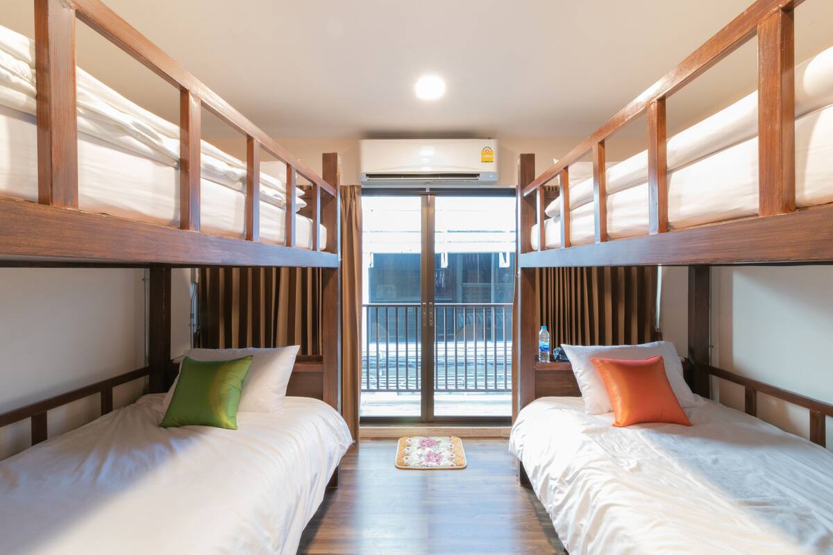 A hotel room with two single beds, wooden headboards, a small rug, and a balcony with a view.