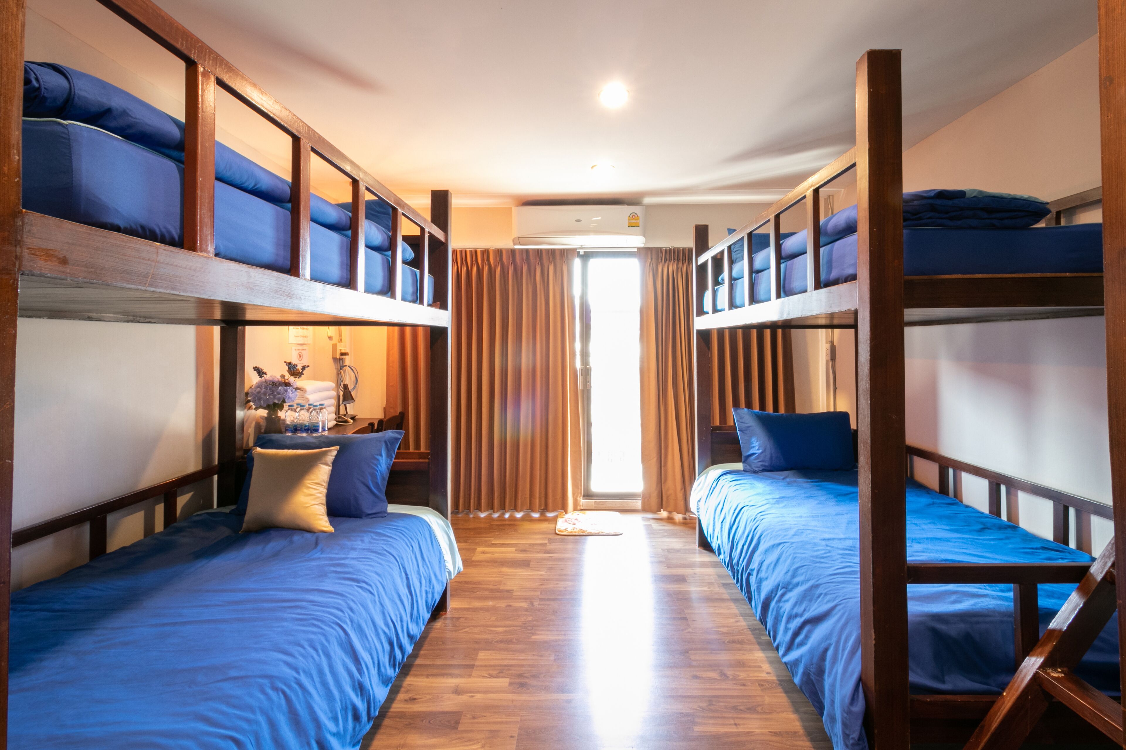 A room with bunk beds, wooden flooring, and a window with curtains.