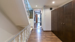 A hallway with wooden flooring, a staircase with white railings, and a large wardrobe on the right. - Phobphanhostel (Bangkok)