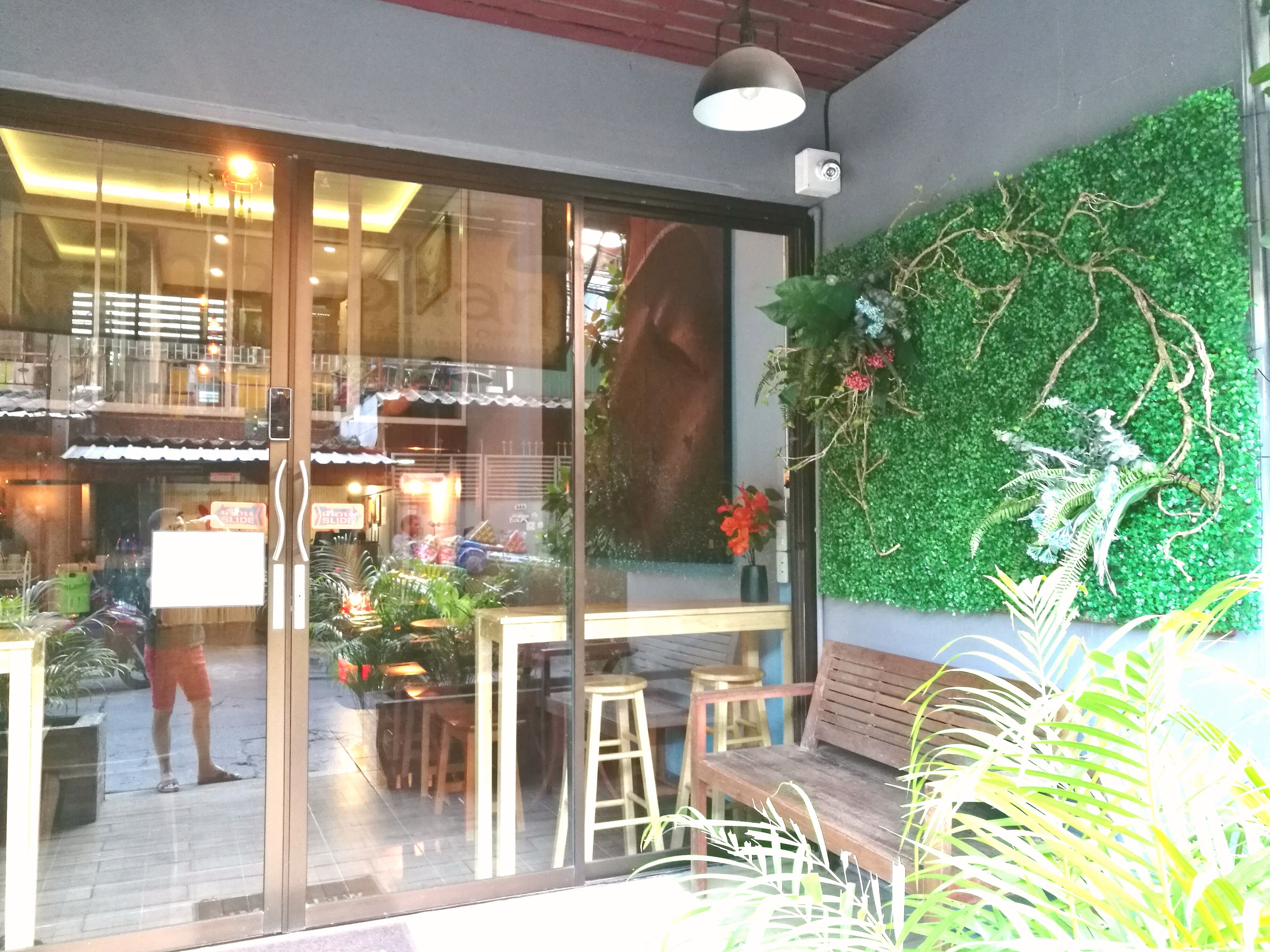 Una cafeteria amb una paret de vidre, plantes d'interior i una banca de fusta.