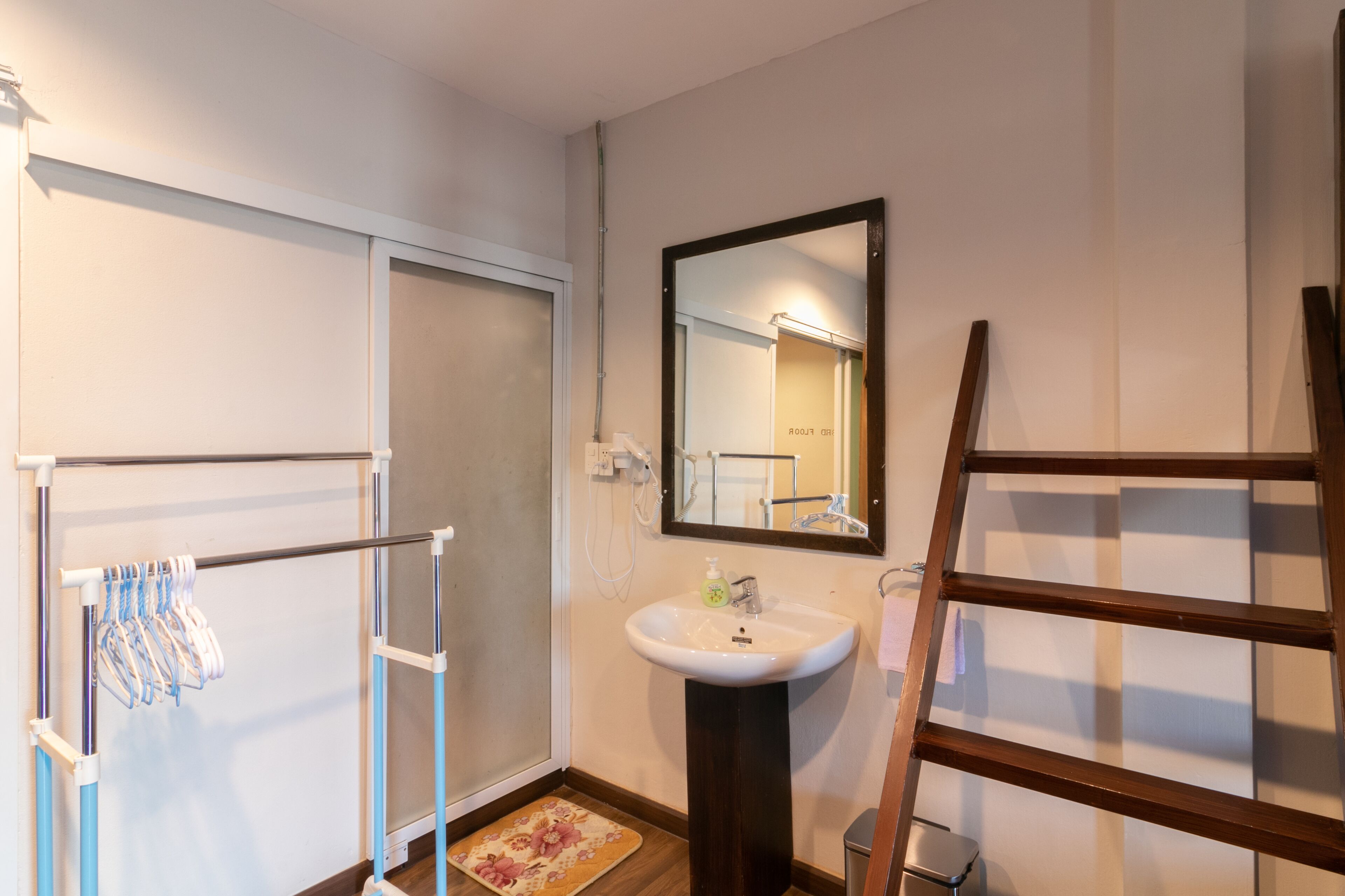 A bathroom with a white sink, a mirror, a towel rack, and a wooden ladder.