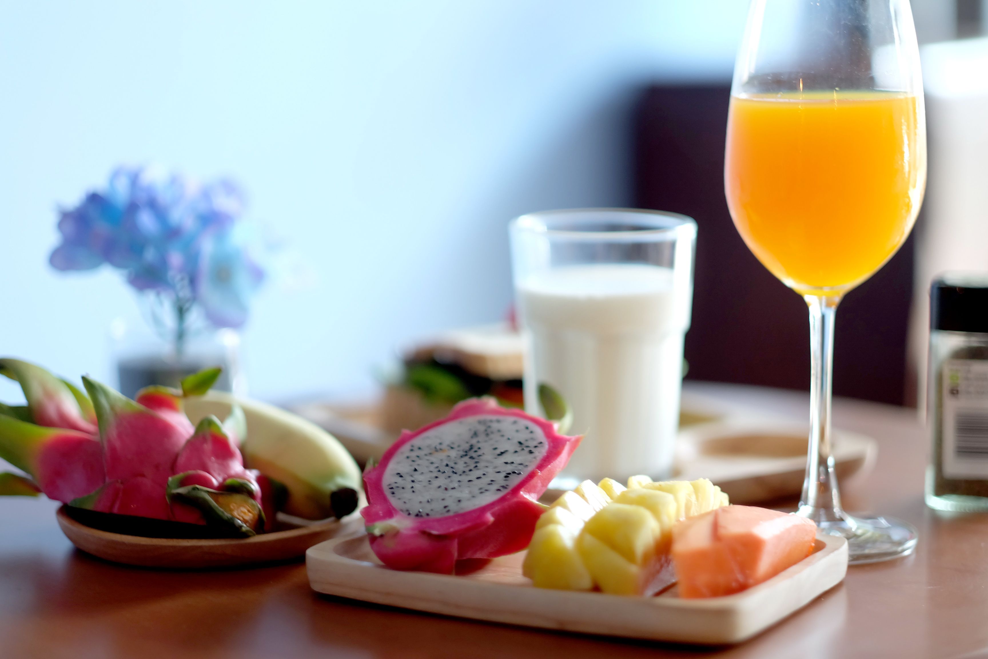 Una colazione con un piatto di pitahaya, mango e salmone, un bicchiere di succo d'arancia e un bicchiere di latte.