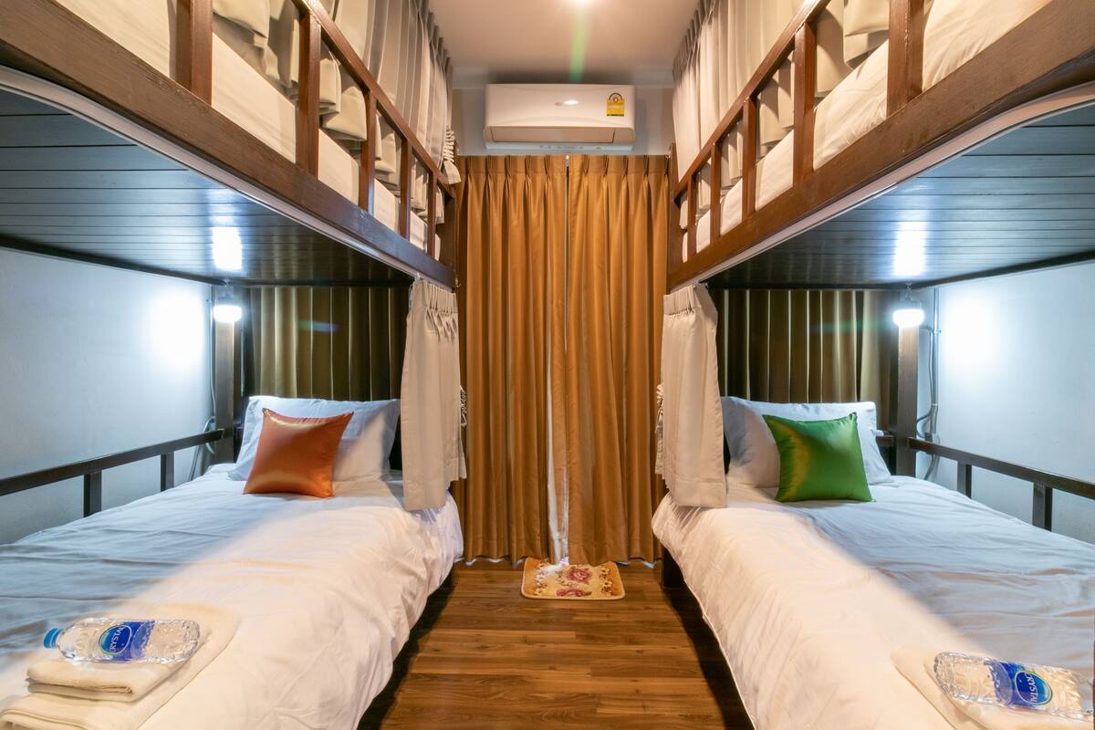 A bunk bed room with a wooden floor, a curtain, and a ceiling fan.
