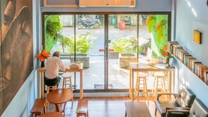 A cafe with a large glass door, wooden furniture, and a view of the street outside. - Phobphanhostel (Bangkok)