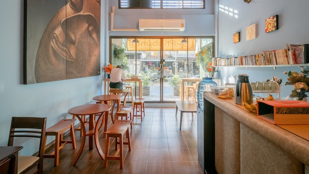 A café with wooden furniture, a large Buddha painting, and a view of the street outside. - Phobphanhostel (Bangkok)