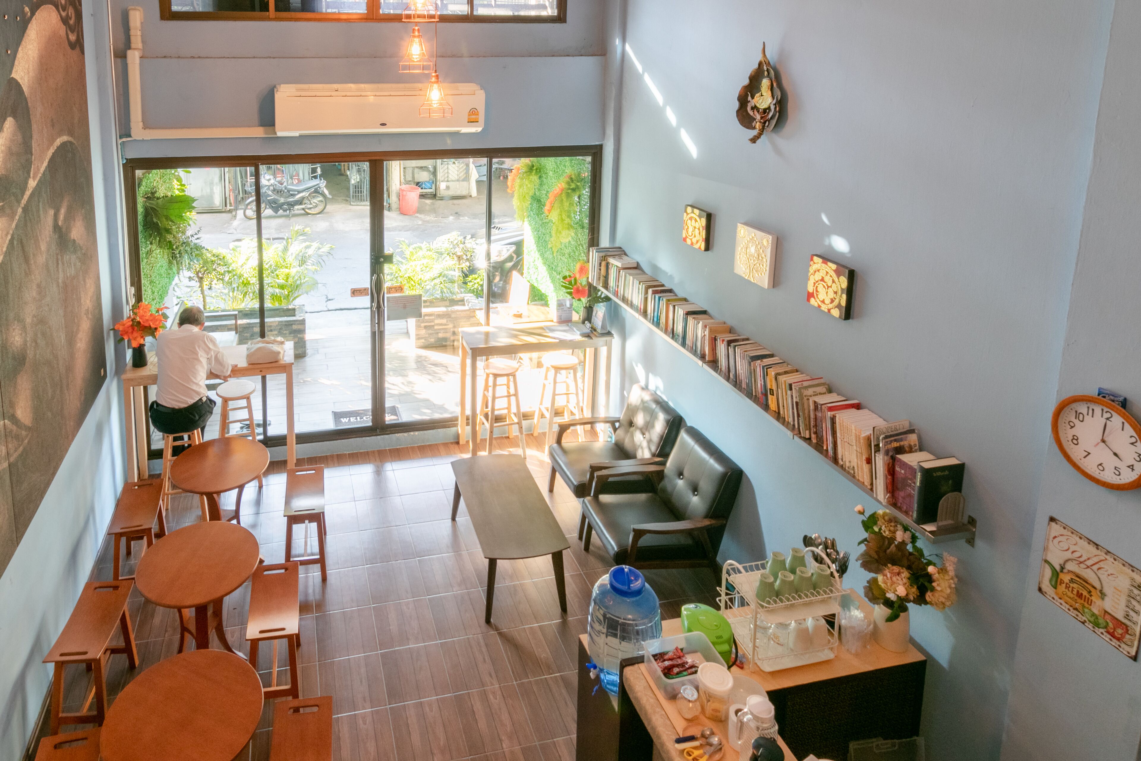 Um café com mesas e bancos de madeira, um balcão com dispensador de água e vista para a rua.