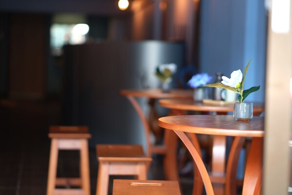 A restaurant interior with wooden tables and chairs, a small vase with flowers, and a blurred background.