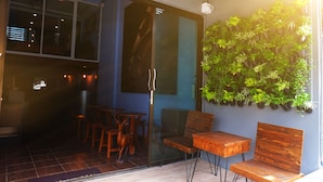 A cozy indoor seating area with wooden furniture, a glass door leading to a balcony, and a wall-mounted plant display. - Phobphanhostel (Bangkok)