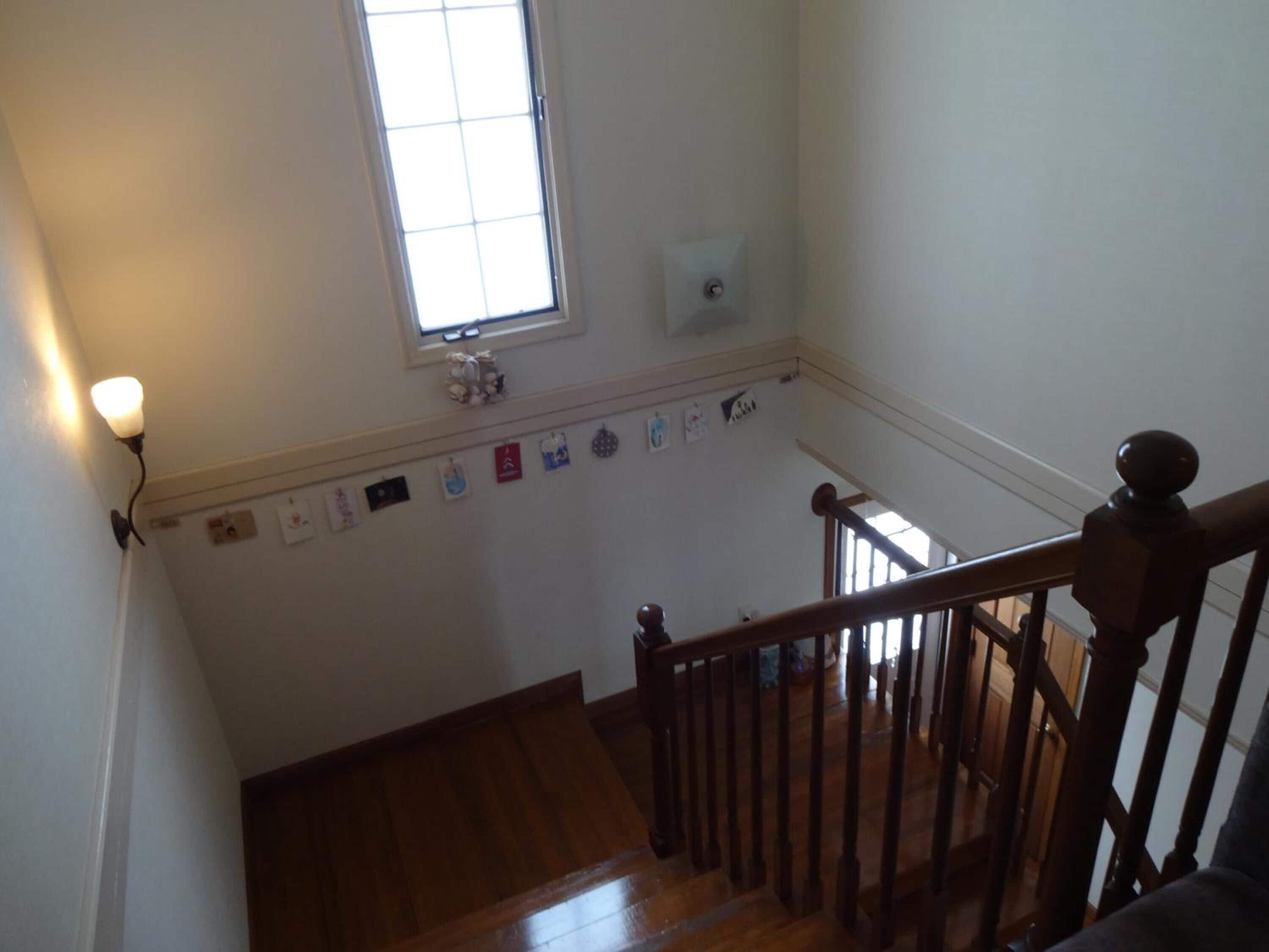 A staircase with wooden railings and a handrail, leading to a landing with a wall-mounted light fixture and a window.