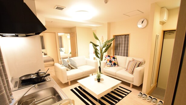 A modern living room with a white sofa, a coffee table, and a kitchen area with a stove and sink. - Matoba biru (Osaka)