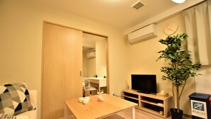 A small, well-lit room with a wooden table, a TV, a plant, and a trash bin. - Matoba biru (Osaka)