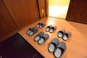 Una fila de zapatillas sobre un suelo de madera en una habitación con paredes y puerta de madera.