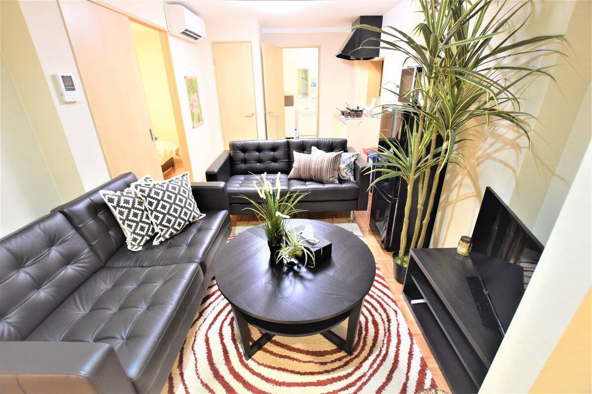 Ein Wohnzimmer mit einer schwarzen Ledersofa, einem runden Couchtisch und einer großen Pflanze.