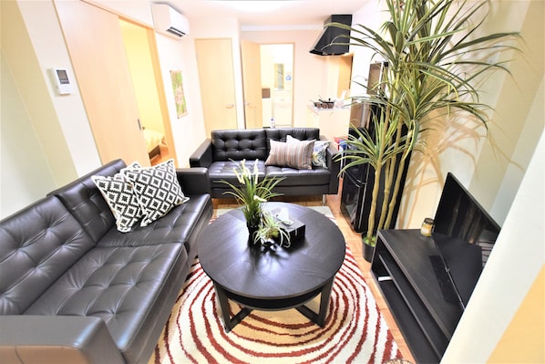Un salón con un sofá de cuero negro, una mesa de centro redonda y una planta grande.